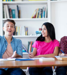 Trois jeunes gens assis à une table, un jeune homme lève la main